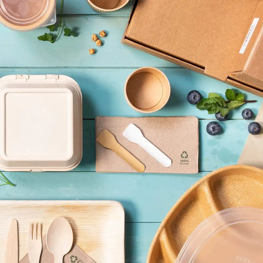 Un assortimento di contenitori per alimenti ecologici, posate e guarnizioni su una superficie blu.