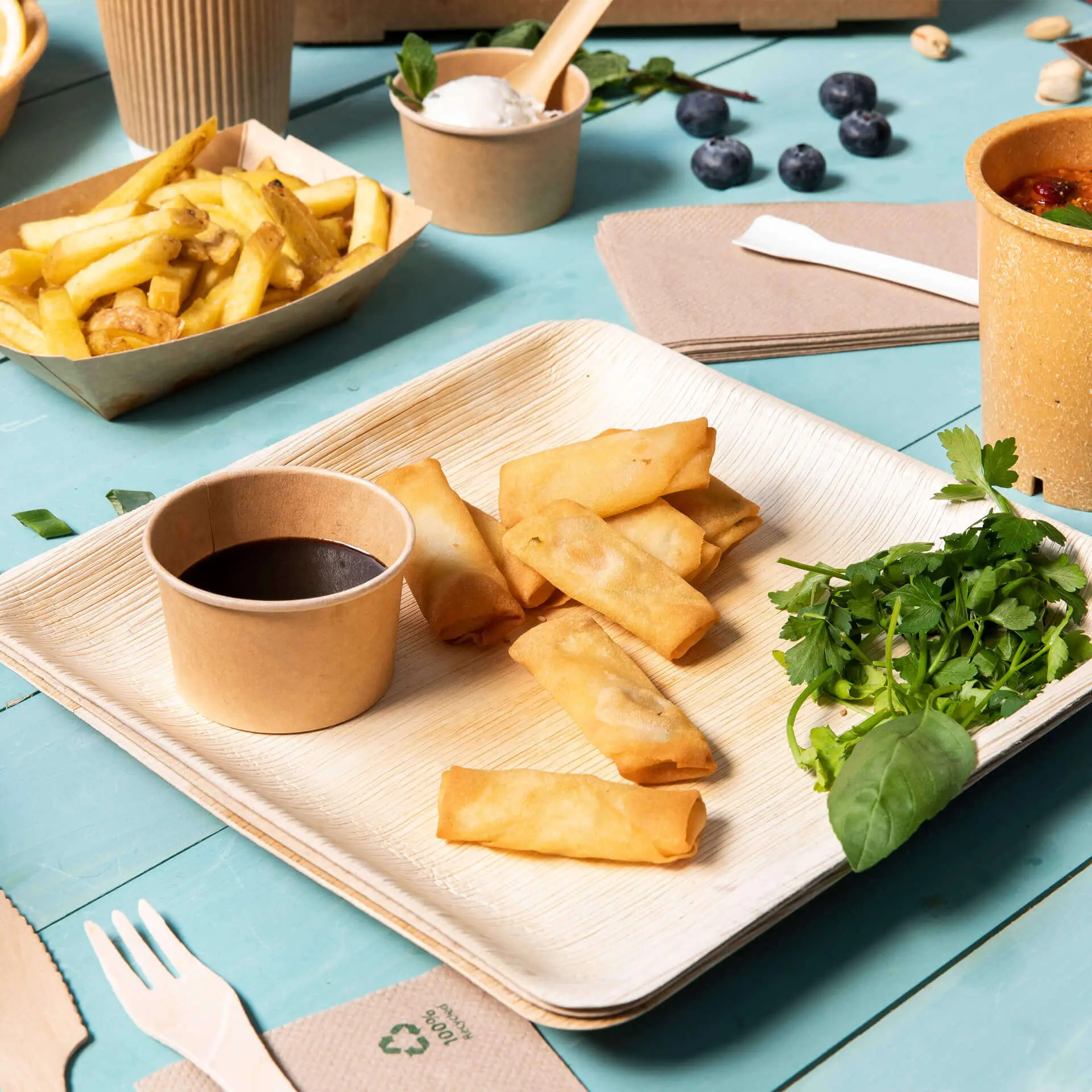 Sei involucri primavera disposti su un piatto quadrato in foglia di palma; accompagnati da una piccola ciotola di salsa e erbe fresche.