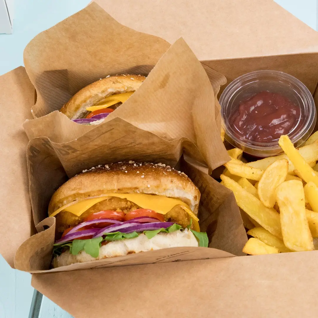 Due burger con formaggio, lattuga, pomodoro e cipolla in una scatola da asporto, accompagnati da patatine e un piccolo contenitore di ketchup.