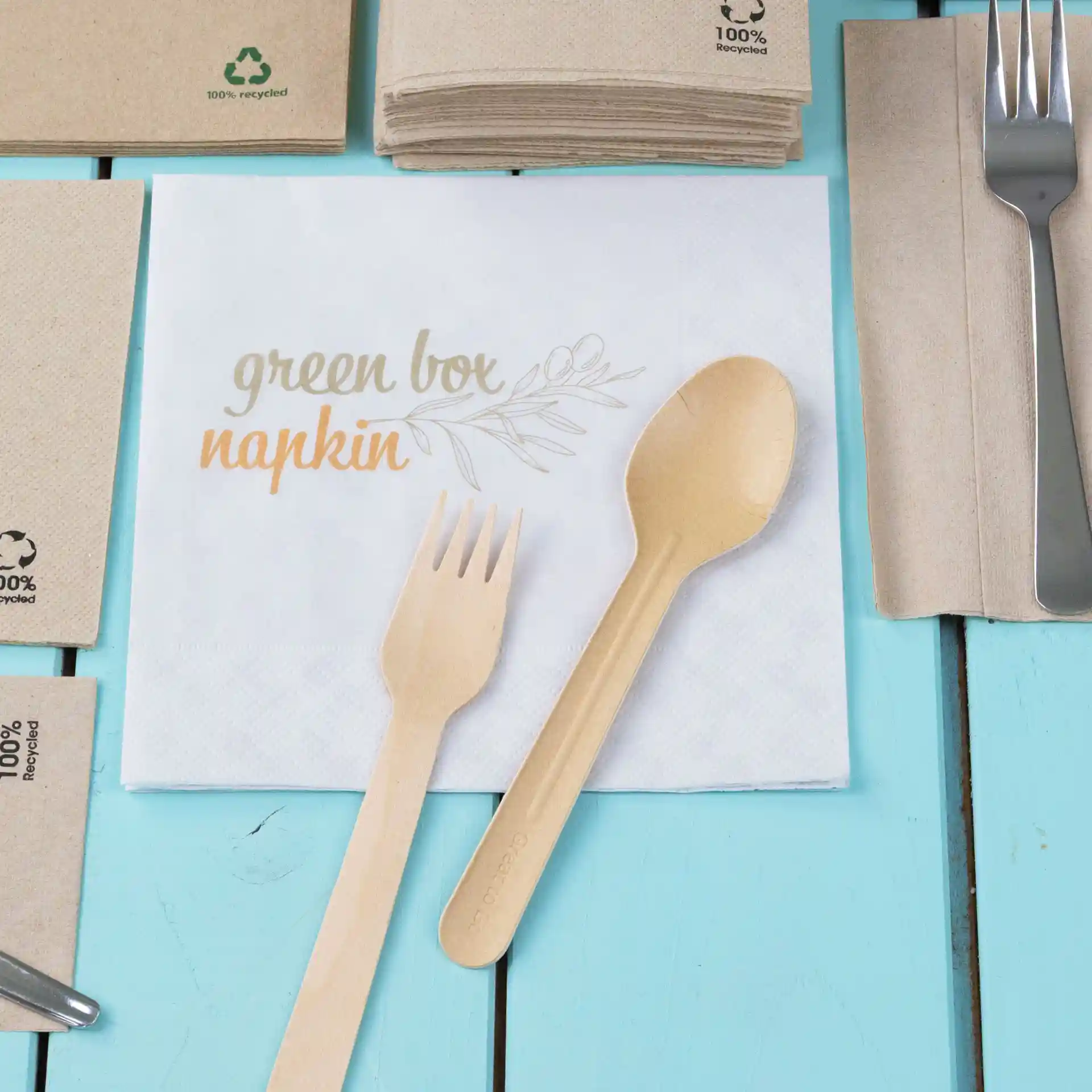 Tovagliolo bianco stampato con il testo "tovagliolo scatola verde", accompagnato da una forchetta e un cucchiaio di legno su una superficie blu.