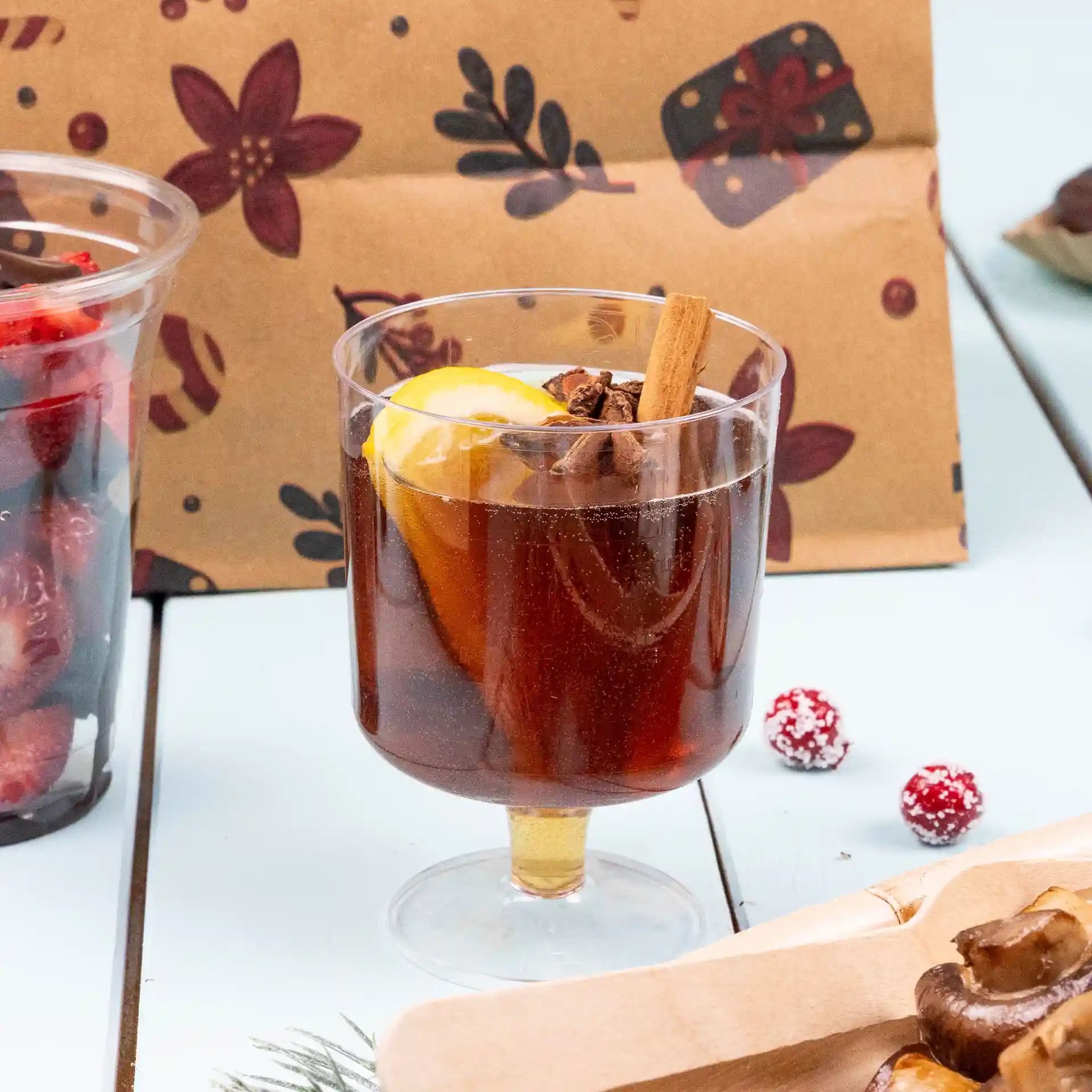 Bicchiere da vino riutilizzabile trasparente riempito con bevanda scura, guarnito con una fetta di limone e un bastoncino di cannella.