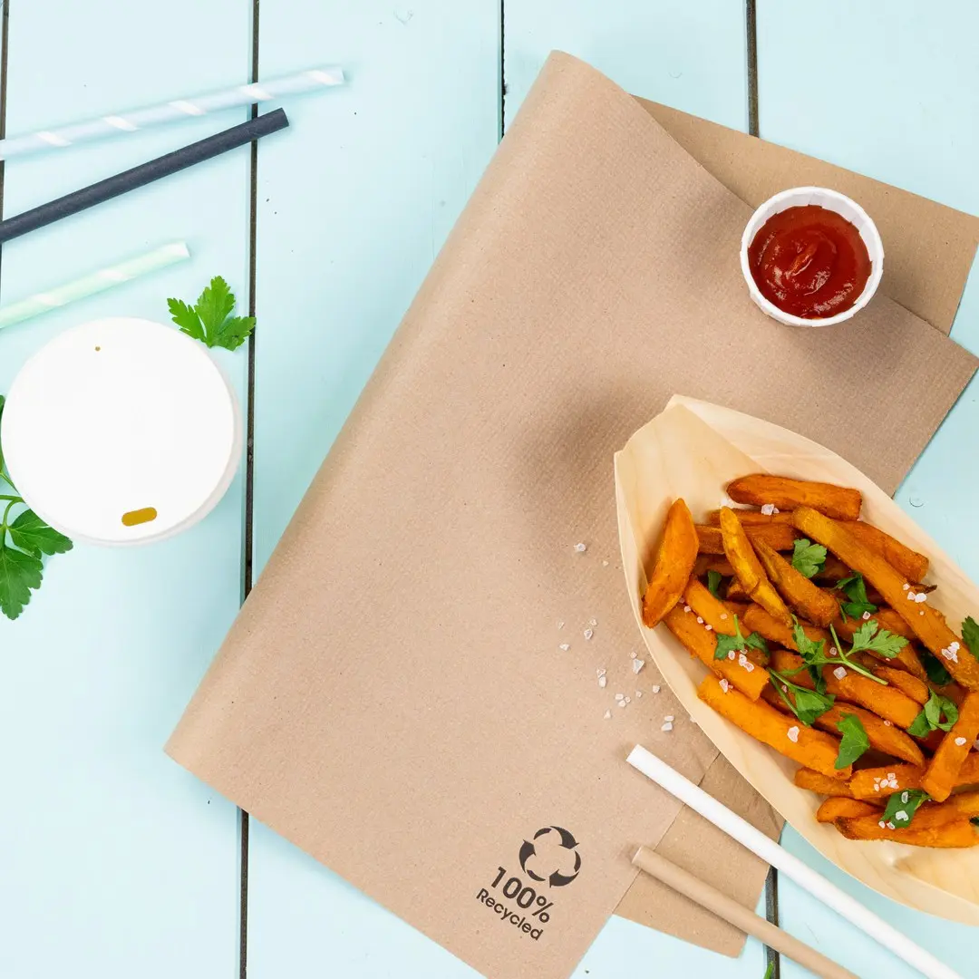 Carta kraft marrone con patatine dolci, ketchup, un bicchiere bianco e cannucce su una superficie in legno blu.