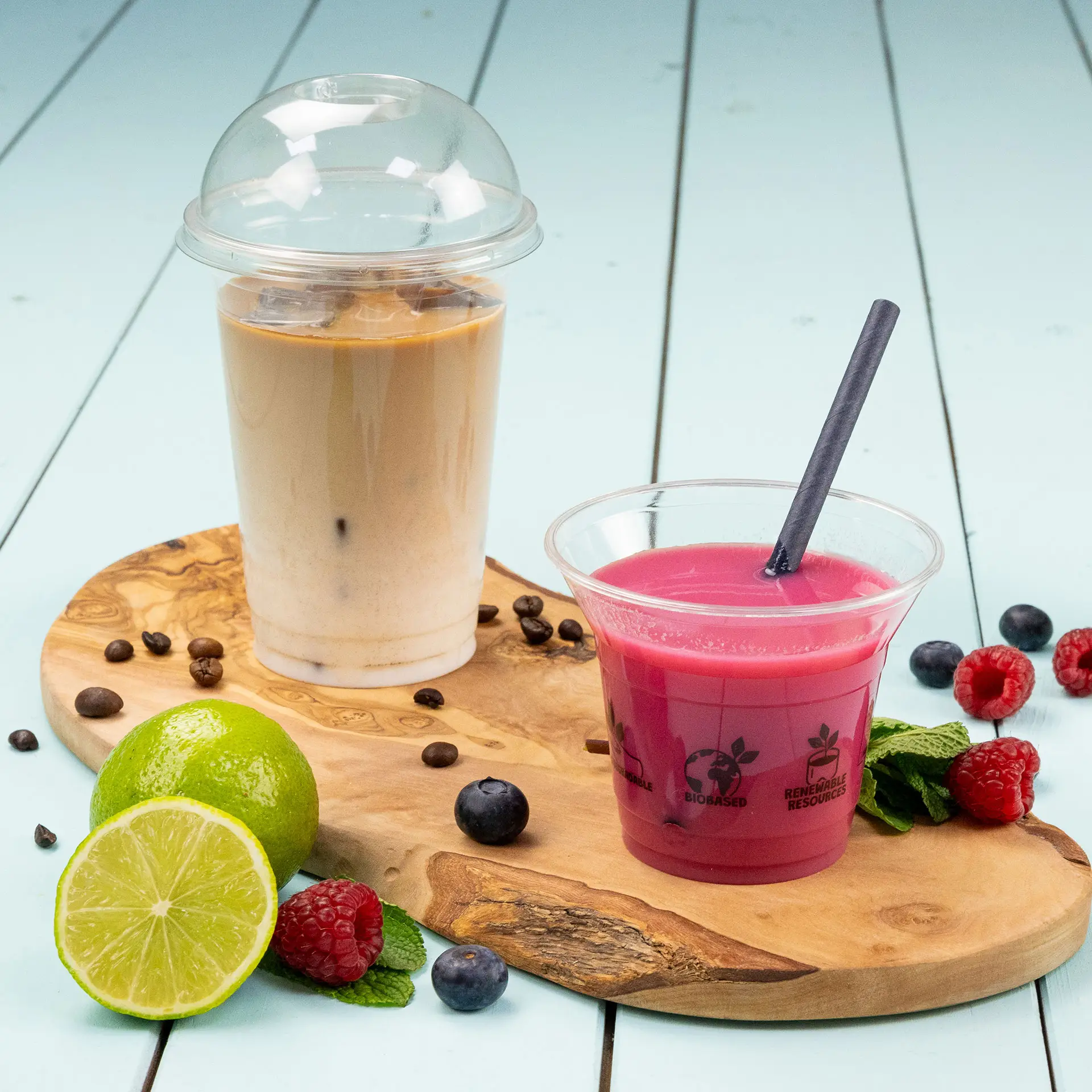 Bicchieri trasparenti pieni di bevande fredde, tra cui caffè freddo e una bevanda rosa, su un tagliere di legno.