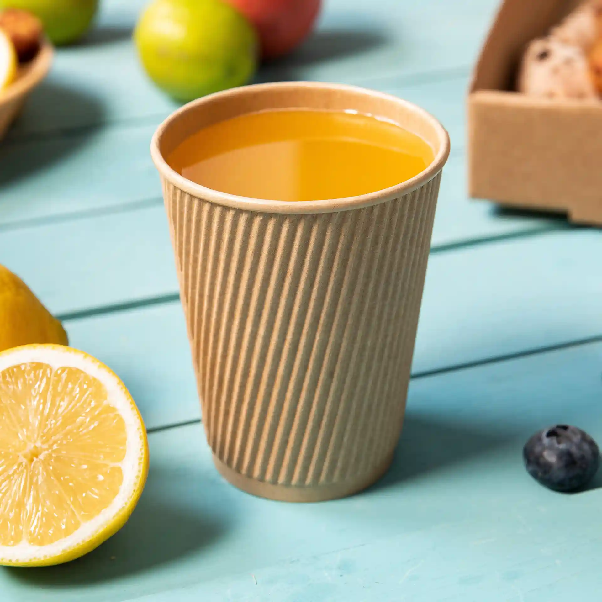 Tazza marrone a righe riempita di liquido giallo, posata su una superficie in legno blu con una metà di limone vicina.