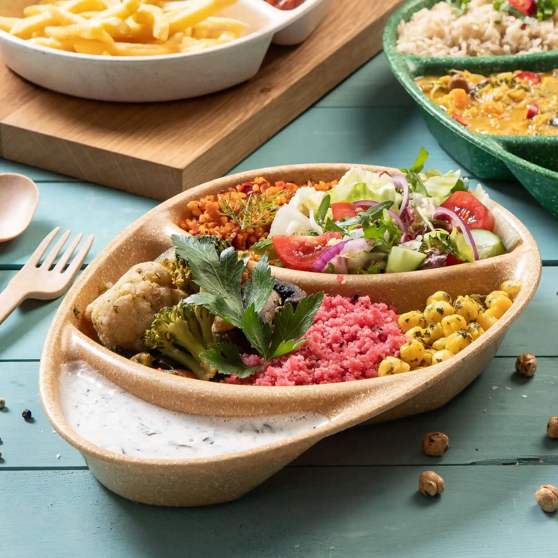 Piatto da menu riutilizzabile con tre scomparti, riempito con vari cibi colorati e una salsa su una superficie blu.