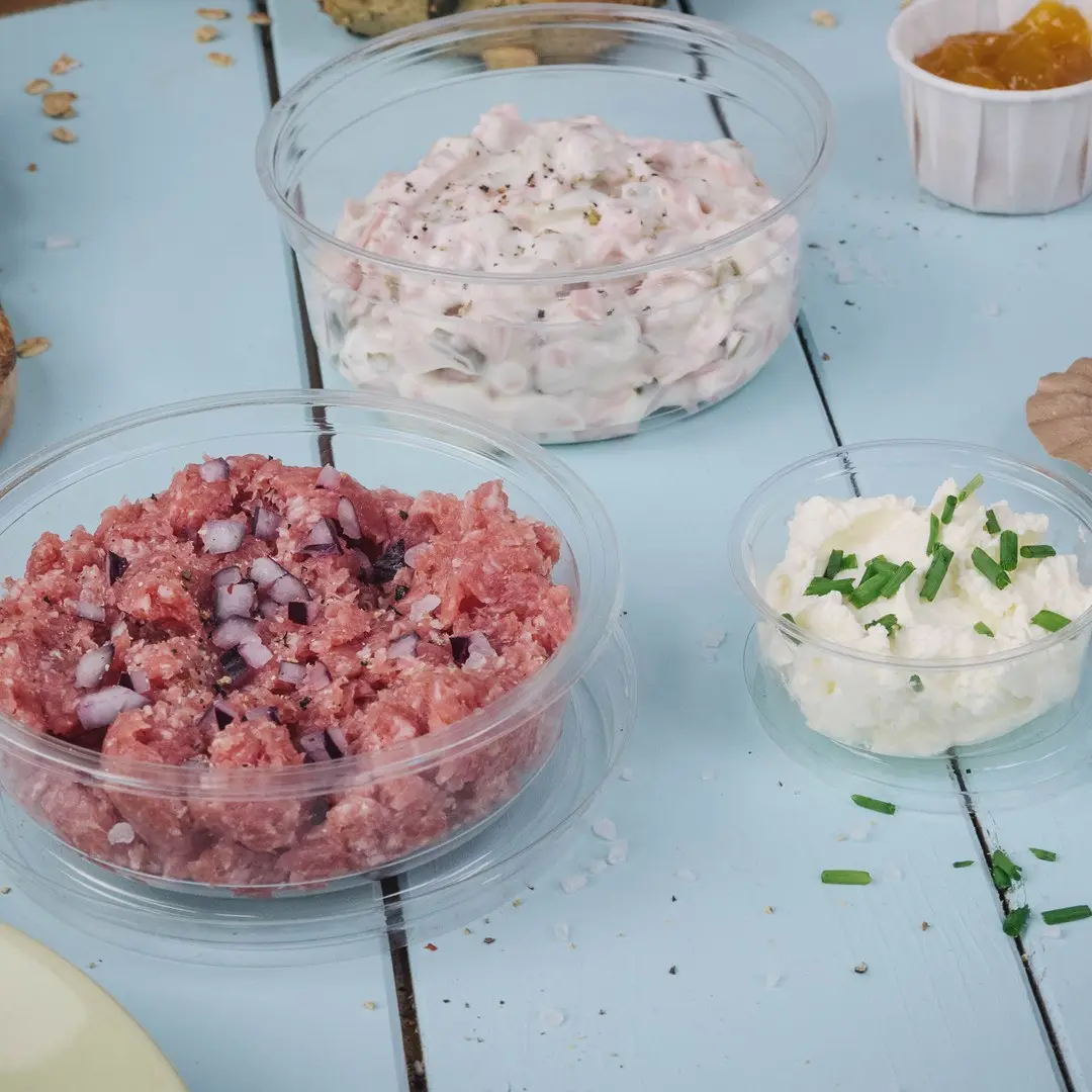 Tre contenitori trasparenti con diverse creme spalmabili: miscela di carne rosa con cipolle, crema bianca cremosa e crema di formaggio bianco con erba cipollina.