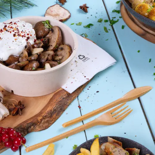 Ciotola con funghi saltati, guarnita con yogurt e spezie, accompagnata da posate di legno su sfondo blu.