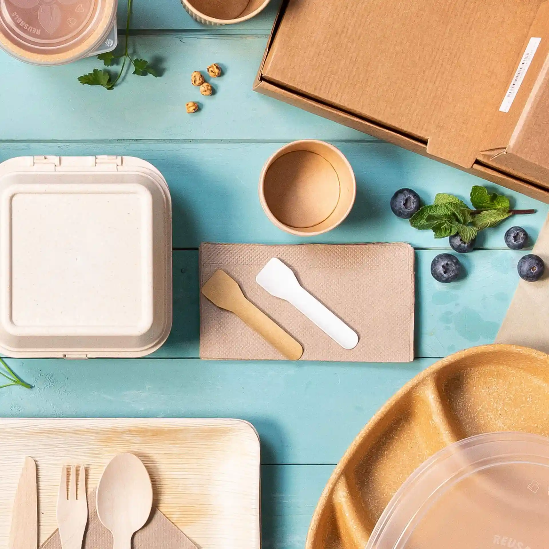 Immagine che mostra vari contenitori alimentari usa e getta, posate e guarnizioni su una superficie blu.