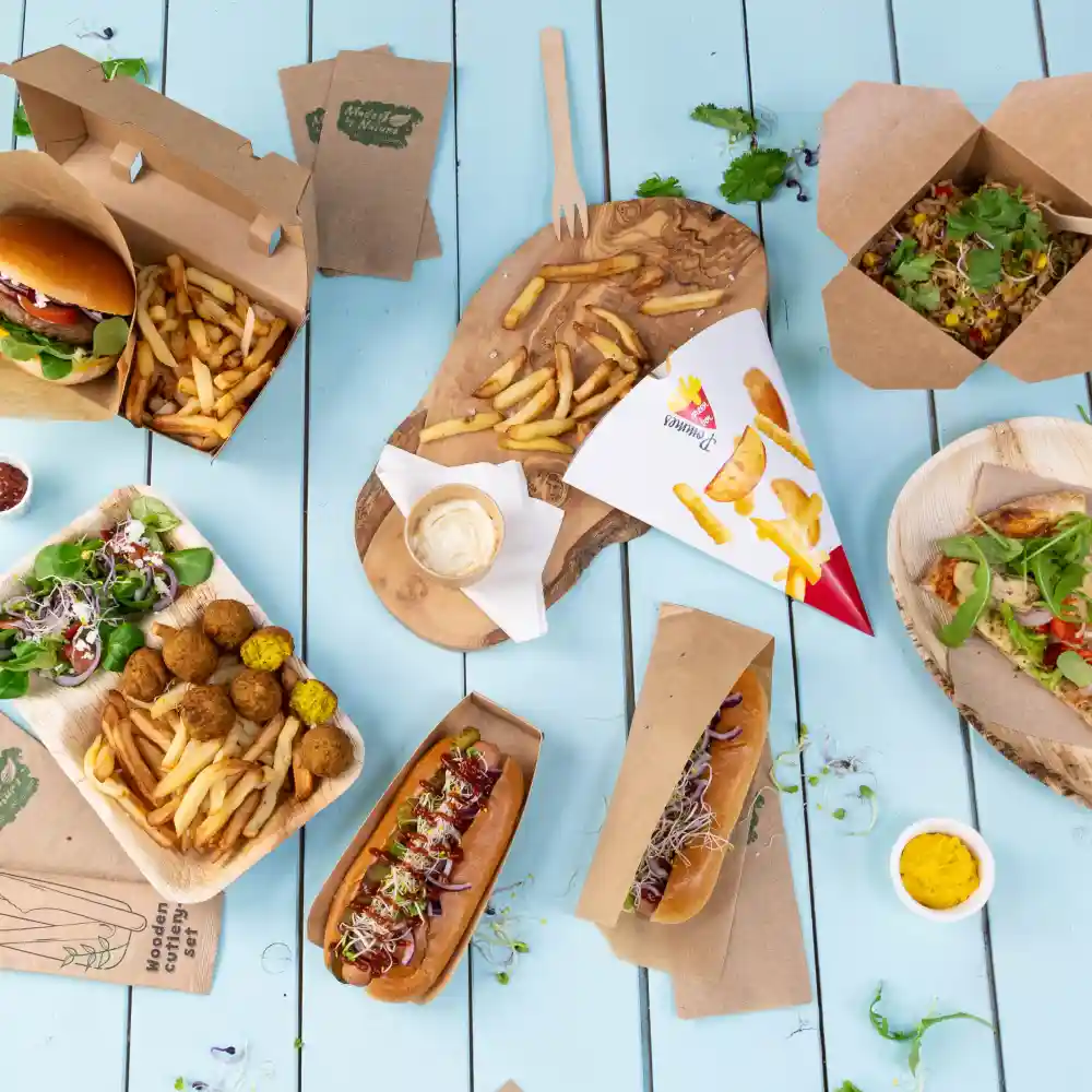 Varietà di cibi da fast food tra cui hamburger, hot dog, patatine, insalata e falafel serviti su vassoi di legno e carta.