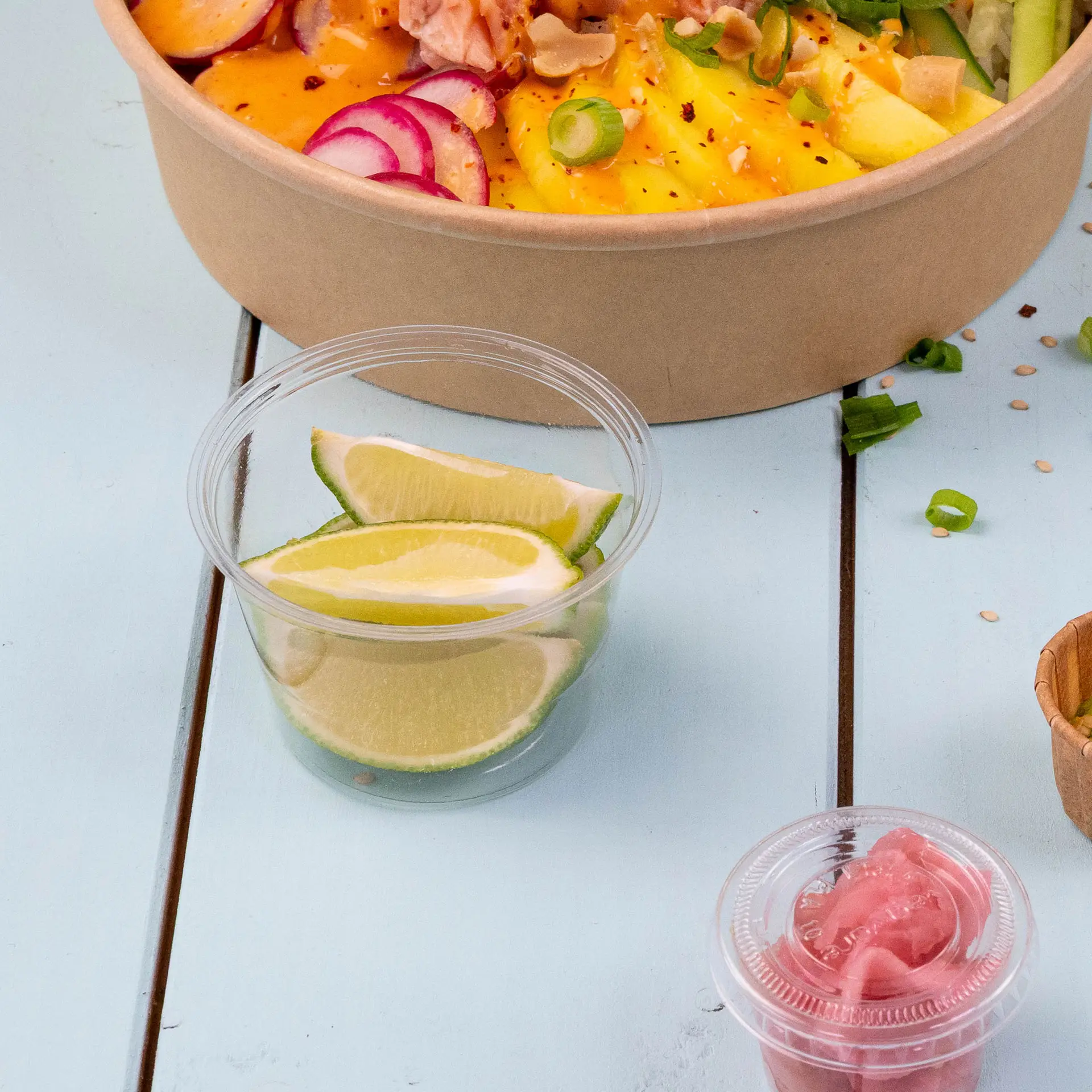 Becher bio in PLA trasparenti con fette di lime per condimenti o salse, posizionati accanto a una ciotola di insalata.
