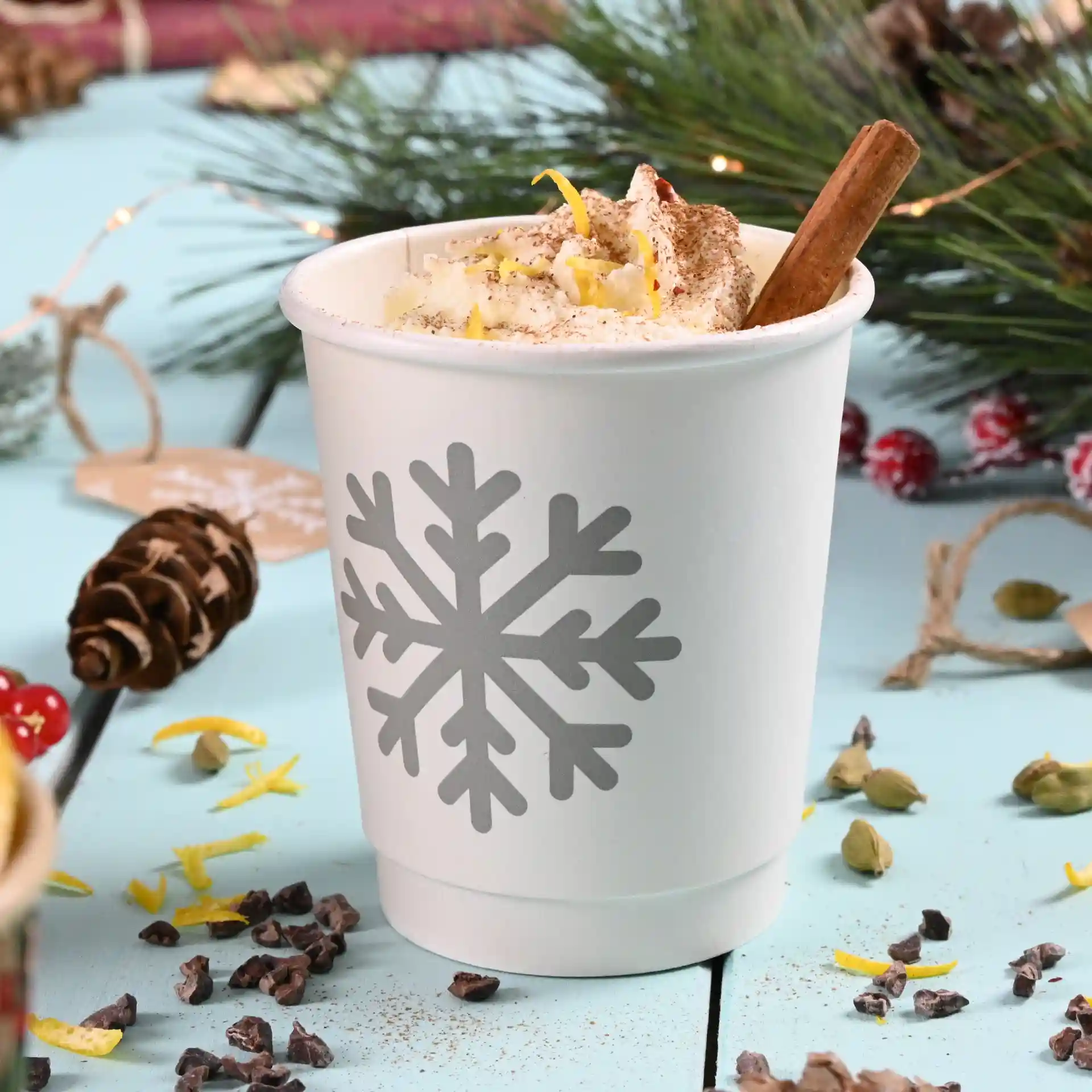 Bicchiere di carta bianco a doppia parete con design di fiocchi di neve grigi, riempito di panna montata e un bastoncino di cannella.