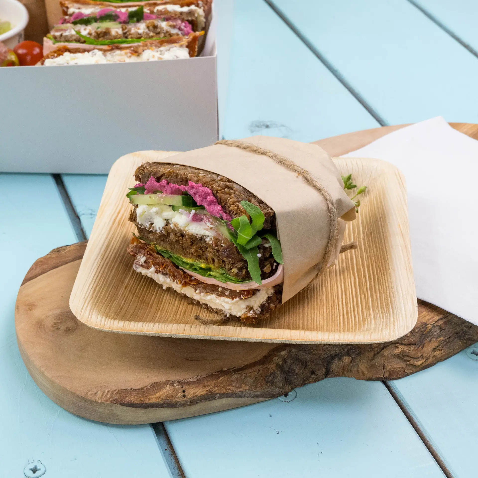 Carta da imballaggio marrone con un panino, con strati di verdure, formaggio cremoso e una crema rosa su un piatto di legno.