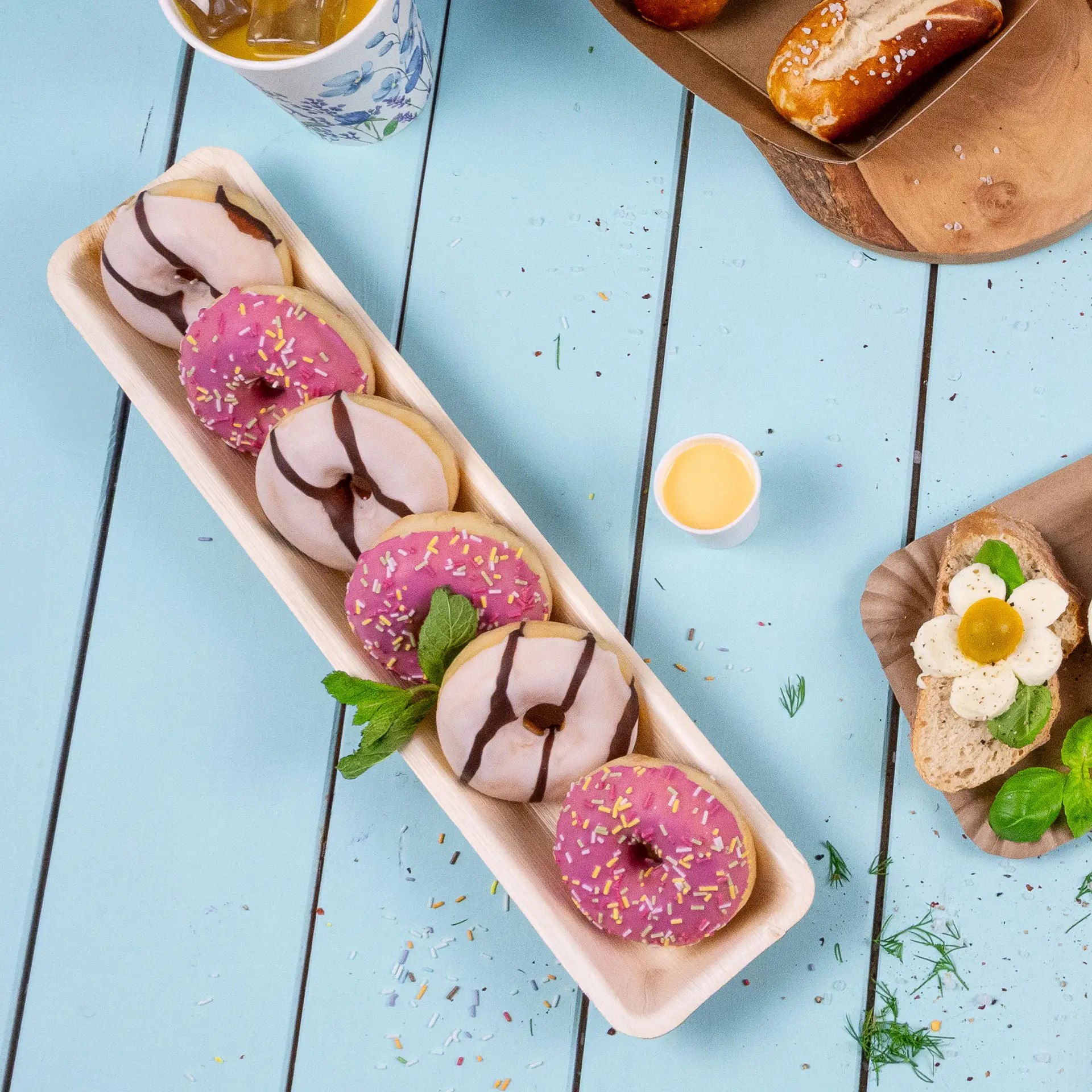 Un vassoio rettangolare in foglie di palma con diversi donut decorati; glassa rosa e bianca con zuccherini.
