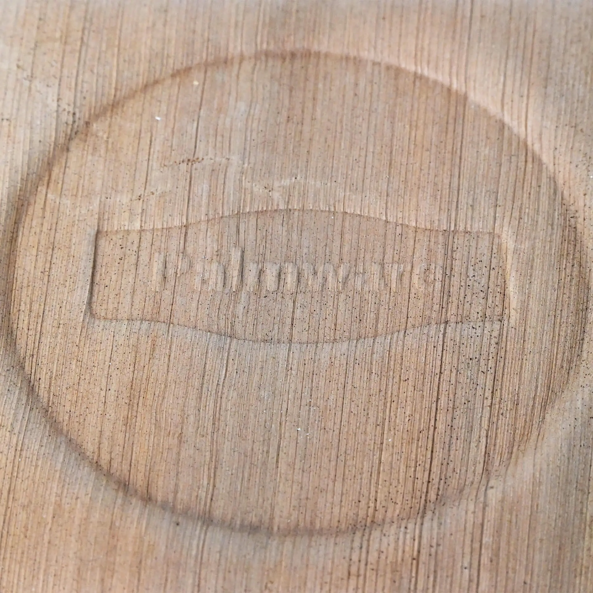 Primo piano di una ciotola in foglia di palma con un'impronta circolare del logo su una superficie in legno.