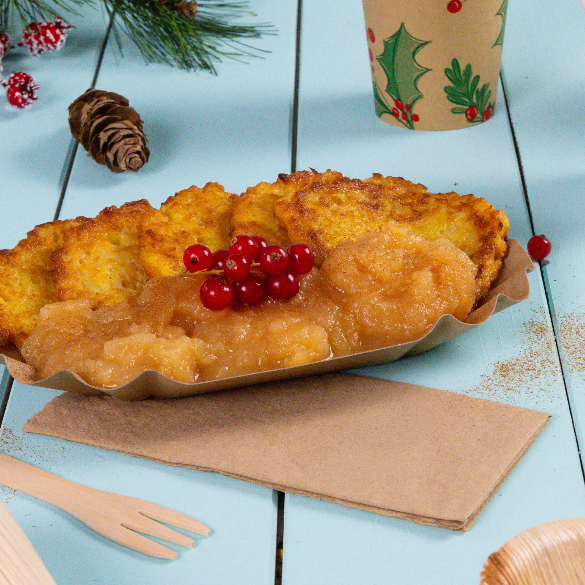 Piatto con diverse frittelle dorate, salsa di mele e ribes rossi, su una superficie in legno blu chiaro con un tovagliolo.