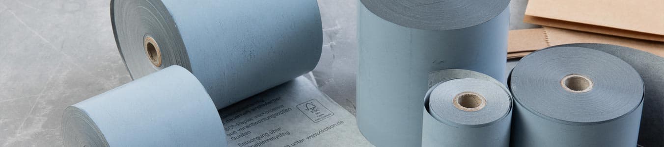 Varie rotoli di carta blu di diverse dimensioni, con un foglio di carta marrone visibile sullo sfondo.