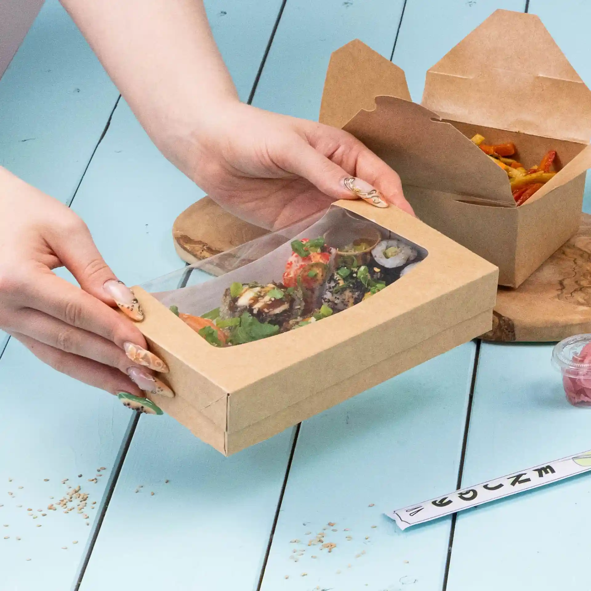 Scatola di cartone con sushi e insalata, con coperchio trasparente, su una superficie blu.