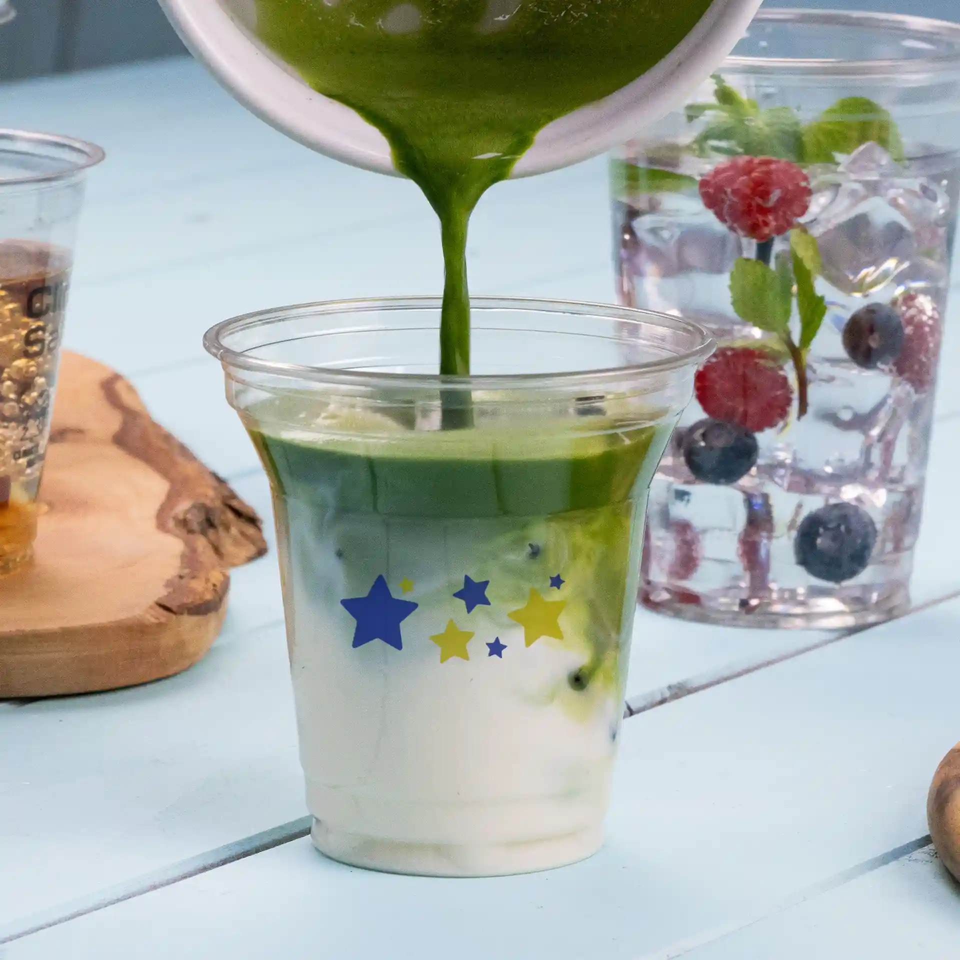 Bicchiere rPET trasparente da 8 oz con design di stelle blu e gialle, riempito di liquido verde e stratificato con bianco.