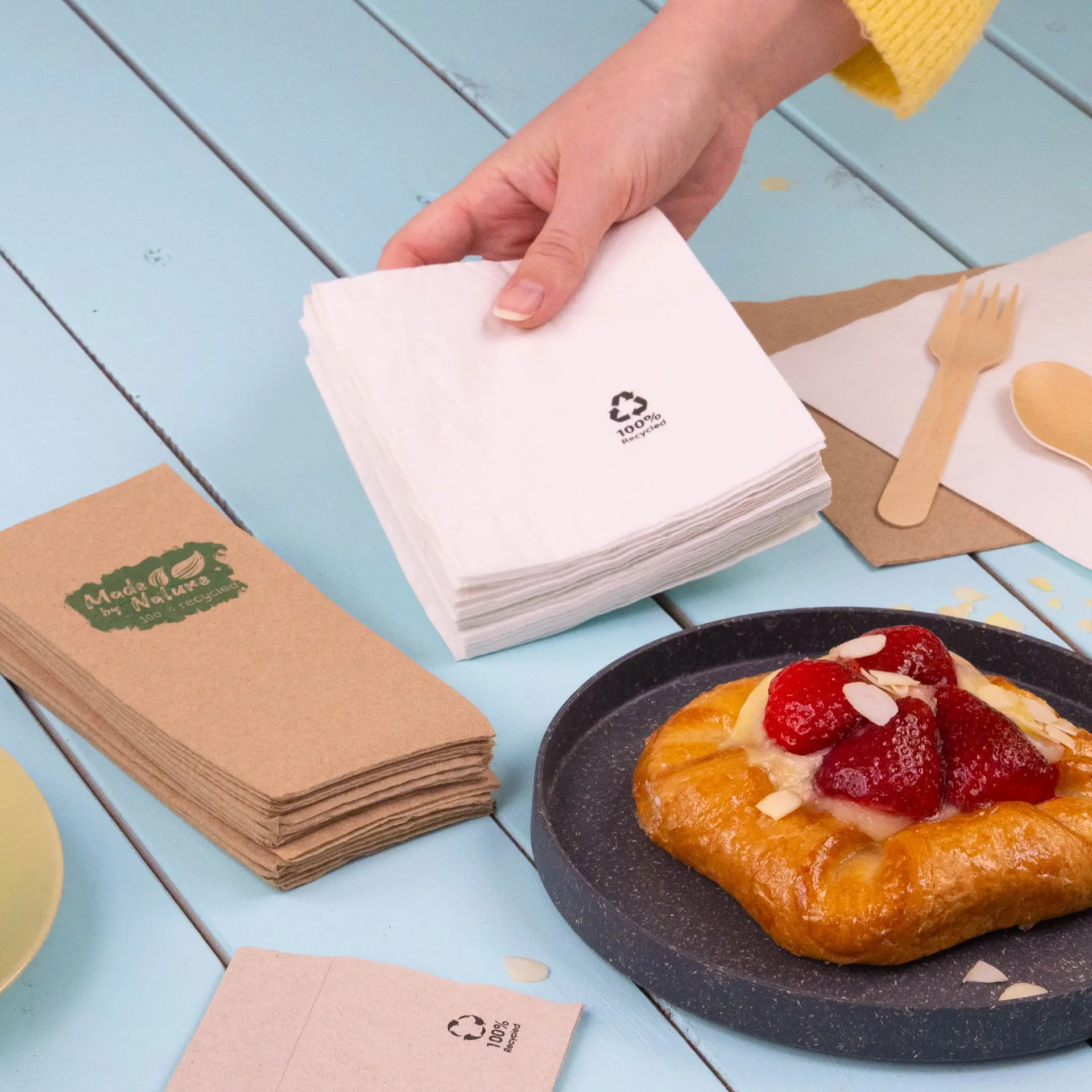 Due tovaglioli da cocktail quadrati, uno bianco e uno grigio chiaro, entrambi in carta riciclata, con simboli di riciclo.