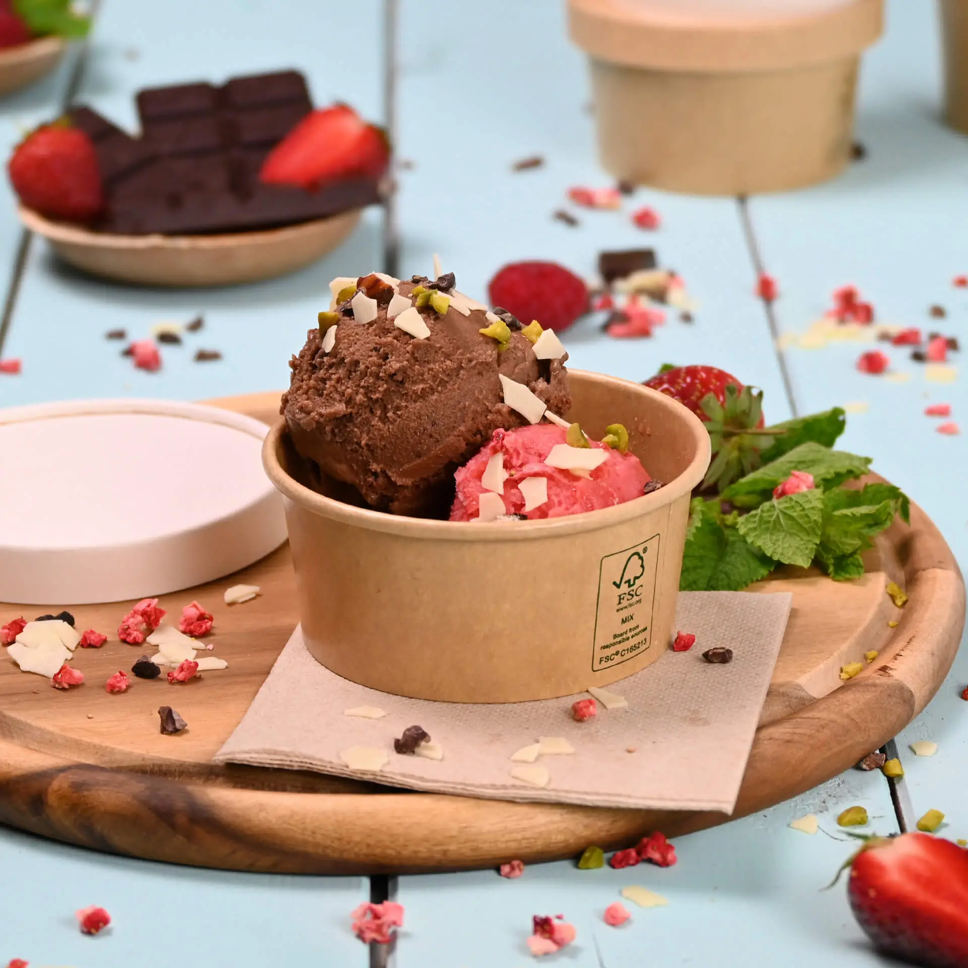 Due palline di gelato al cioccolato e fragola con guarnizioni in un bicchiere di carta marrone; guarnito con menta e fragole.