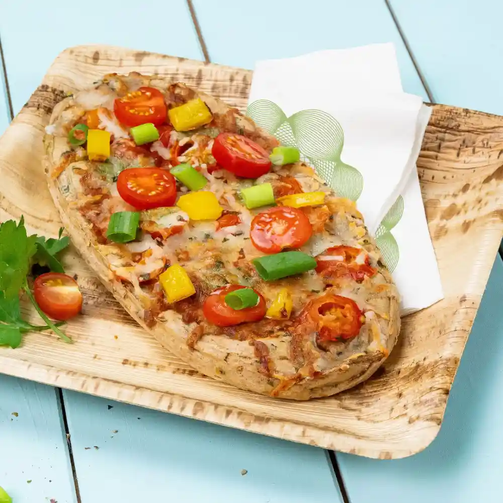 Pizza su pane flatbread guarnita con pomodorini, peperoni e cipollotti, servita su un piatto di legno con tovaglioli.