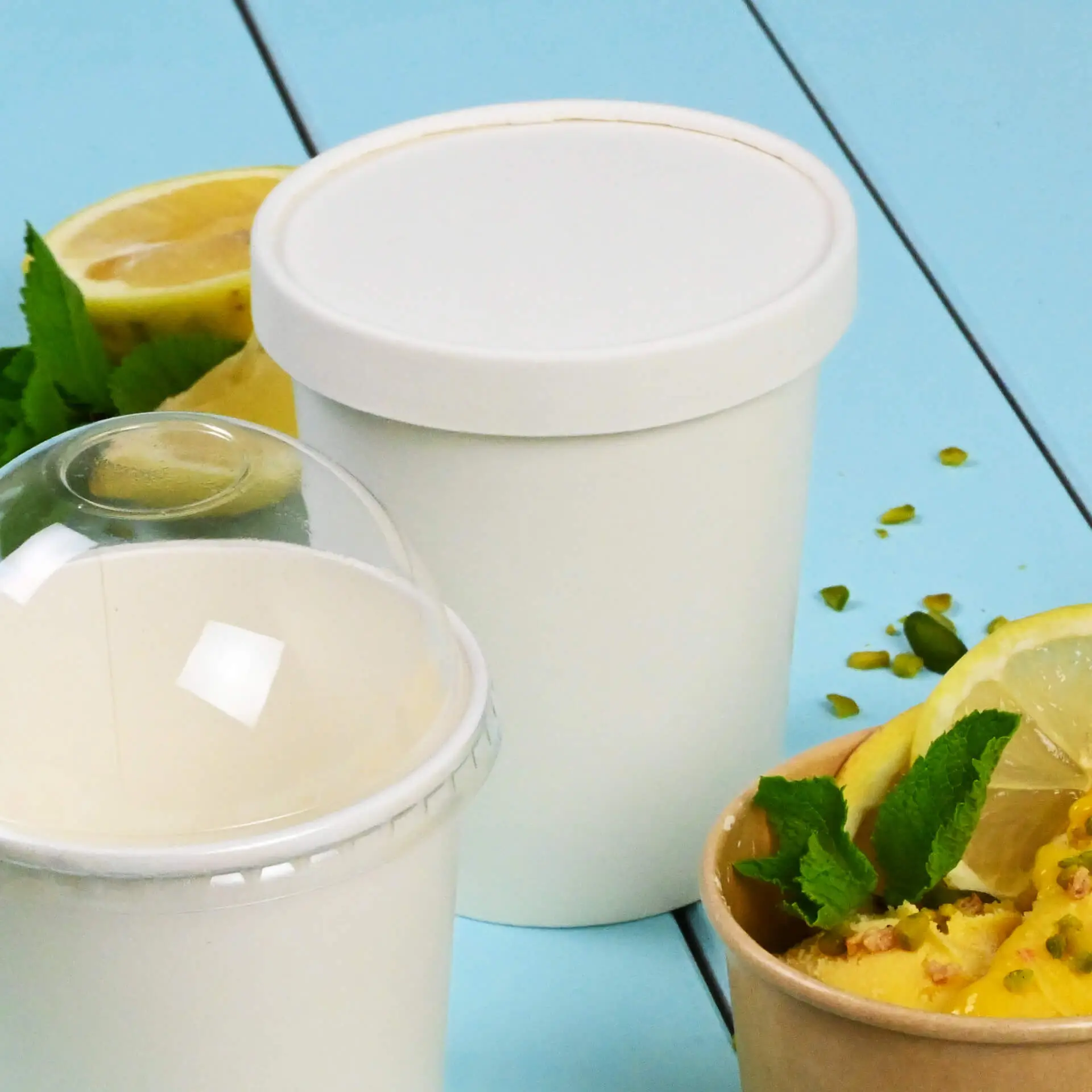 Un coperchio di cartone bianco per coppette di gelato, mostrato con fette di limone e menta; contenitore di gelato aggiuntivo in primo piano.