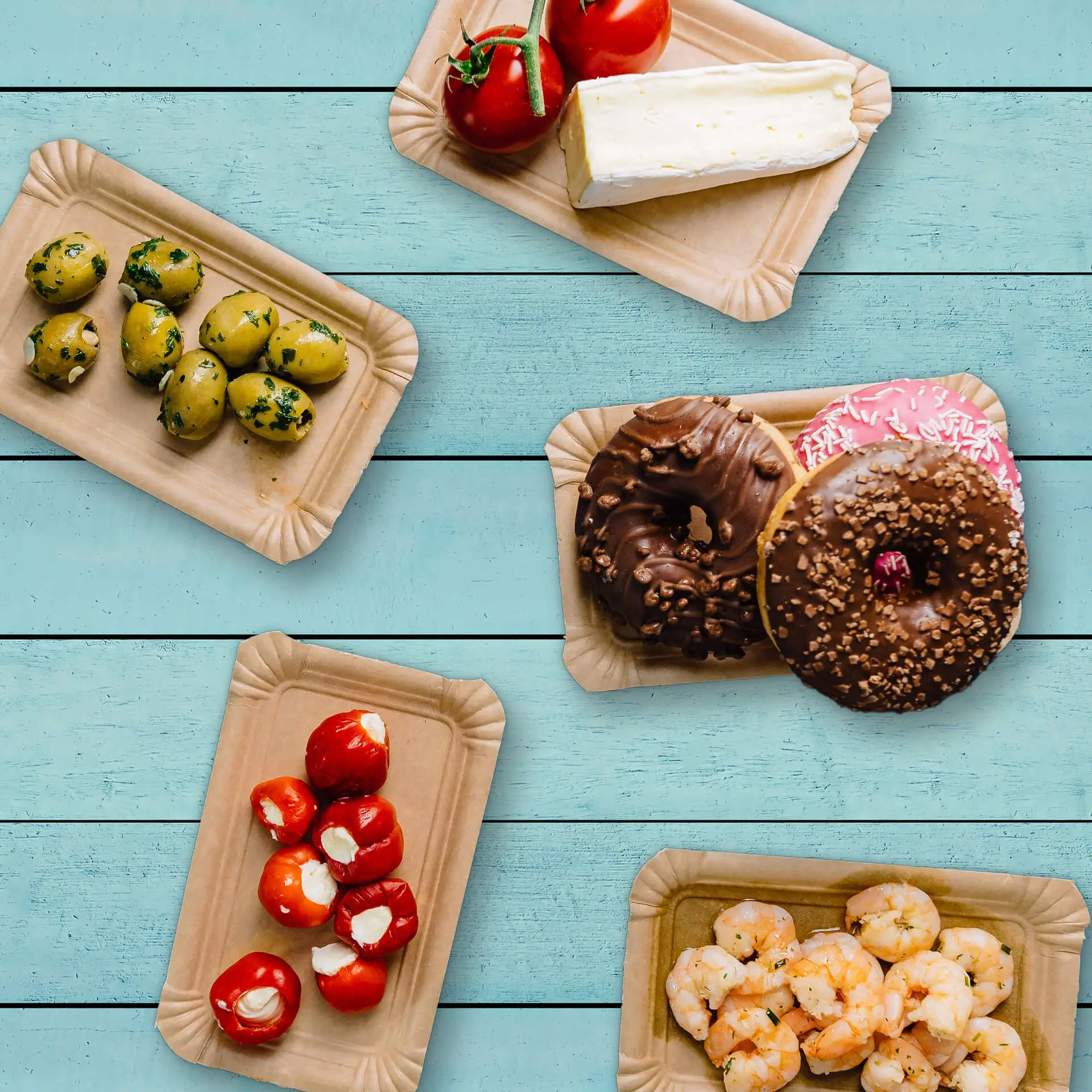 Piatti di cartone con vari alimenti: olive, pomodori, formaggio, gamberi e ciambelle, disposti su uno sfondo azzurro.