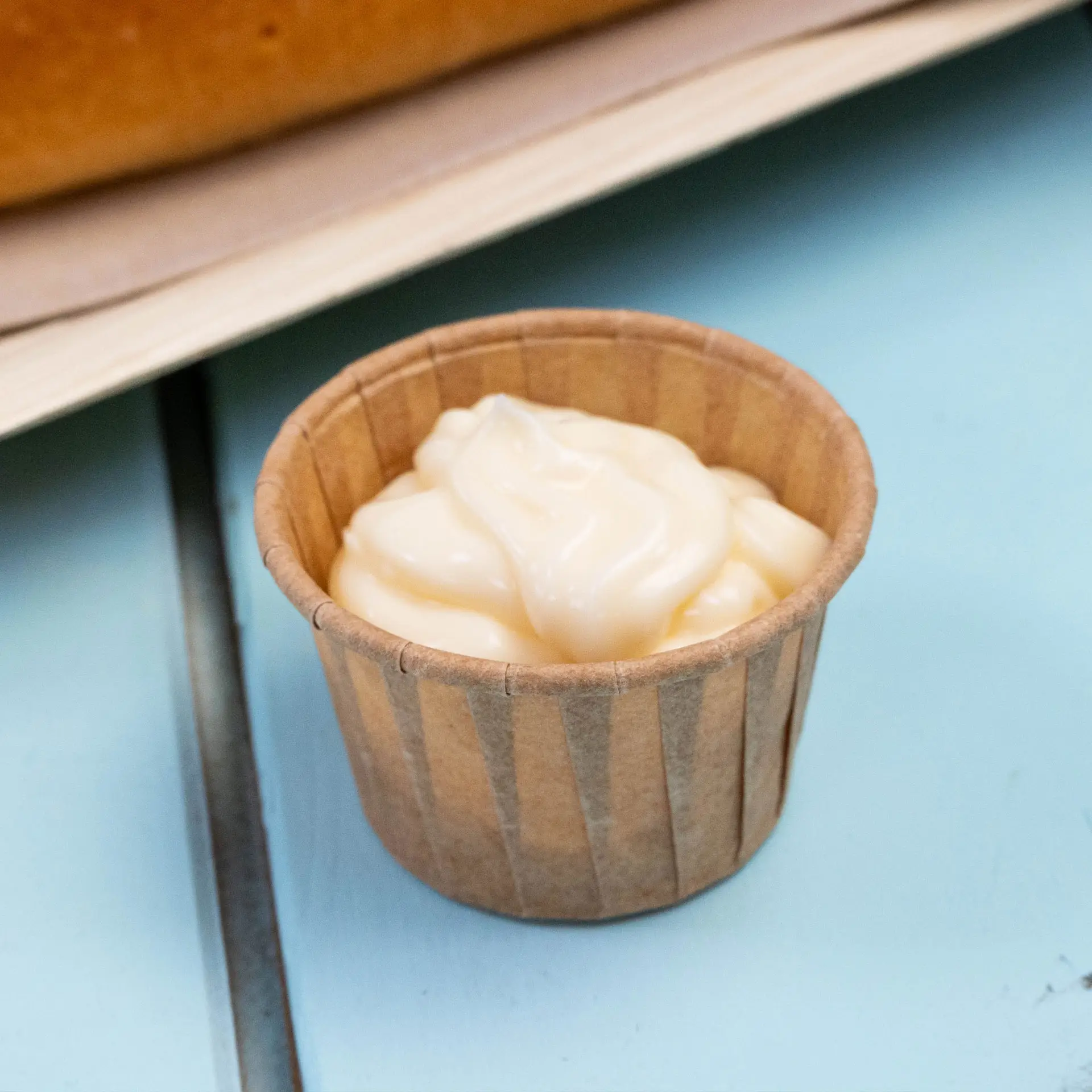 Piccolo bicchiere di carta marrone con un dip cremoso, ideale per salse e porzioni da assaggio, su una superficie blu.