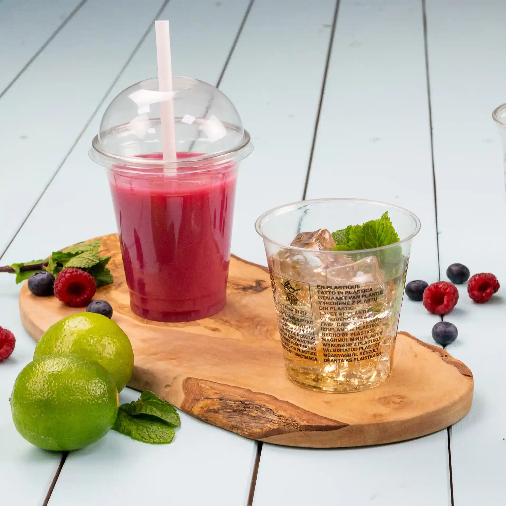 Immagine di un tagliere in legno con un bicchiere trasparente da 12 oz in rPET riempito con una bevanda rosa e un secondo bicchiere chiaro con ghiaccio e menta.