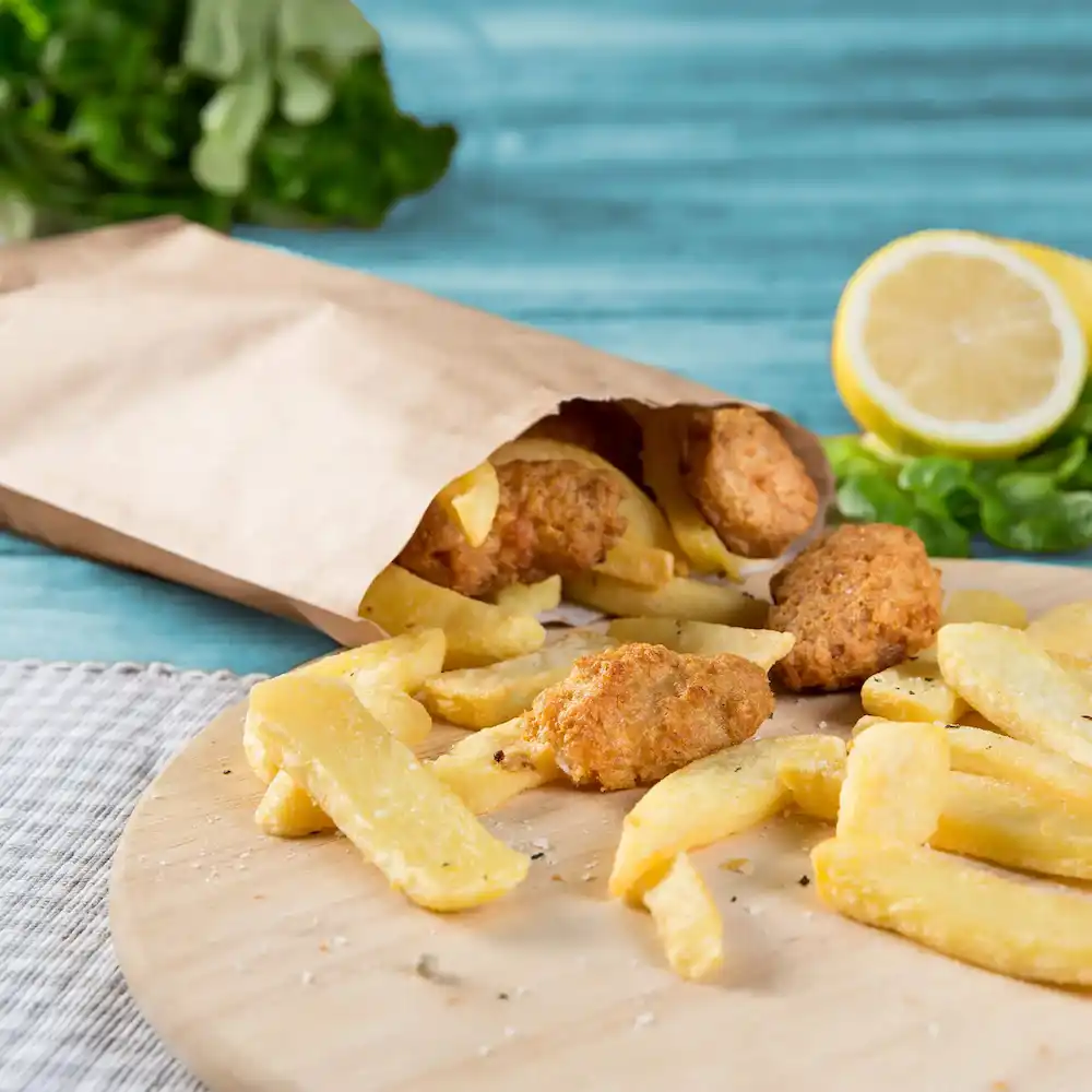 Sacchetto di carta con cibo fritto che esce, con patatine e vari pezzi dorati, limone e vegetazione sullo sfondo.