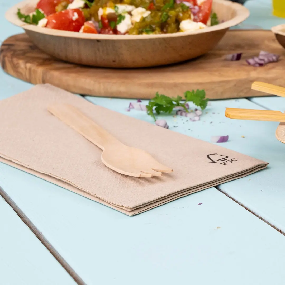 Forchetta di legno posata su un tovagliolo beige piegato, con una ciotola di insalata sullo sfondo su un tavolo azzurro.