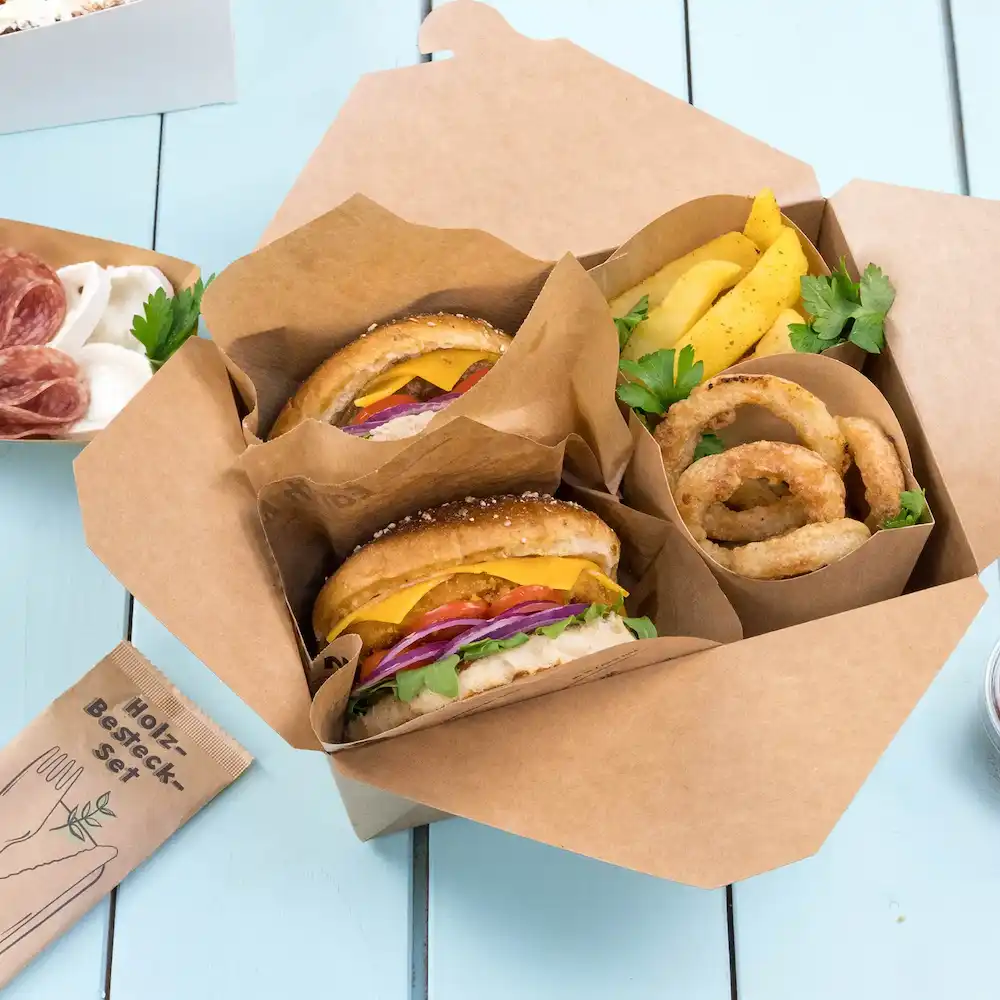 Due hamburger con formaggio, lattuga, pomodoro e cipolla in una scatola da asporto, accompagnati da anelli di cipolla e patatine.