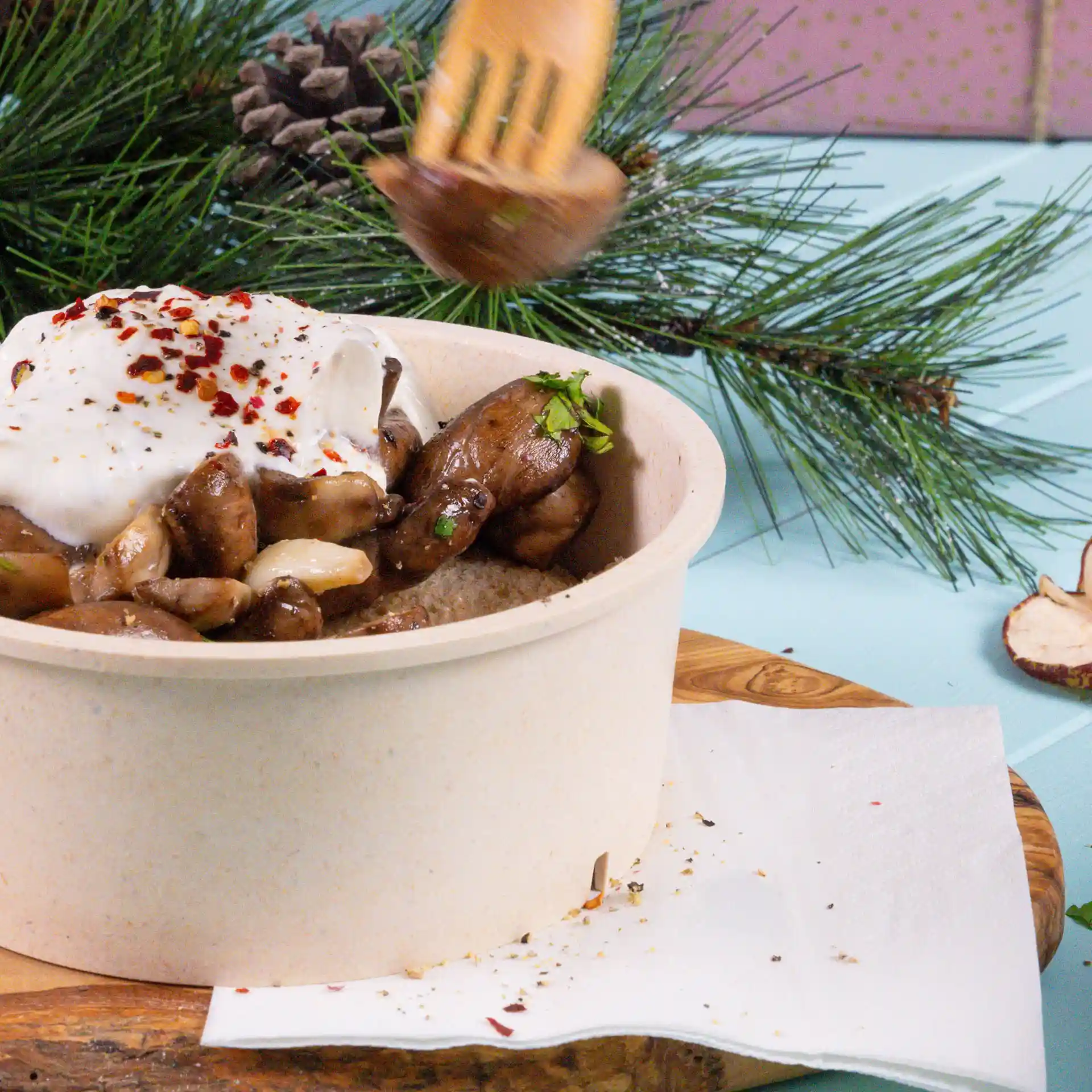 Ciotola con funghi e yogurt, guarnita con fiocchi di peperoncino rosso, posata su un tagliere di legno con un tovagliolo bianco accanto.