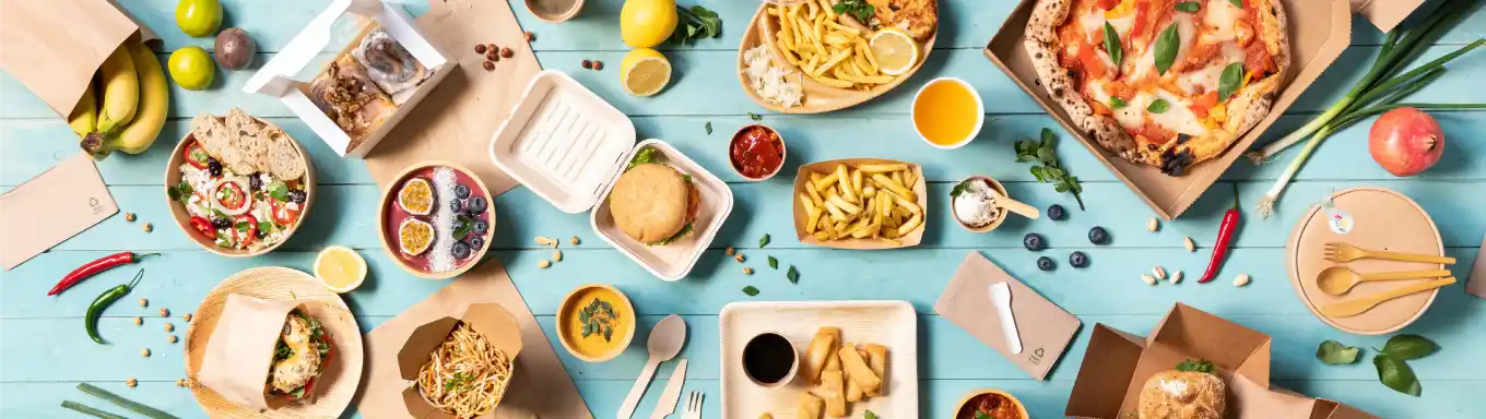 Una varietà di cibi disposti su una superficie blu, tra cui pizza, insalate, hamburger e dolci in contenitori.