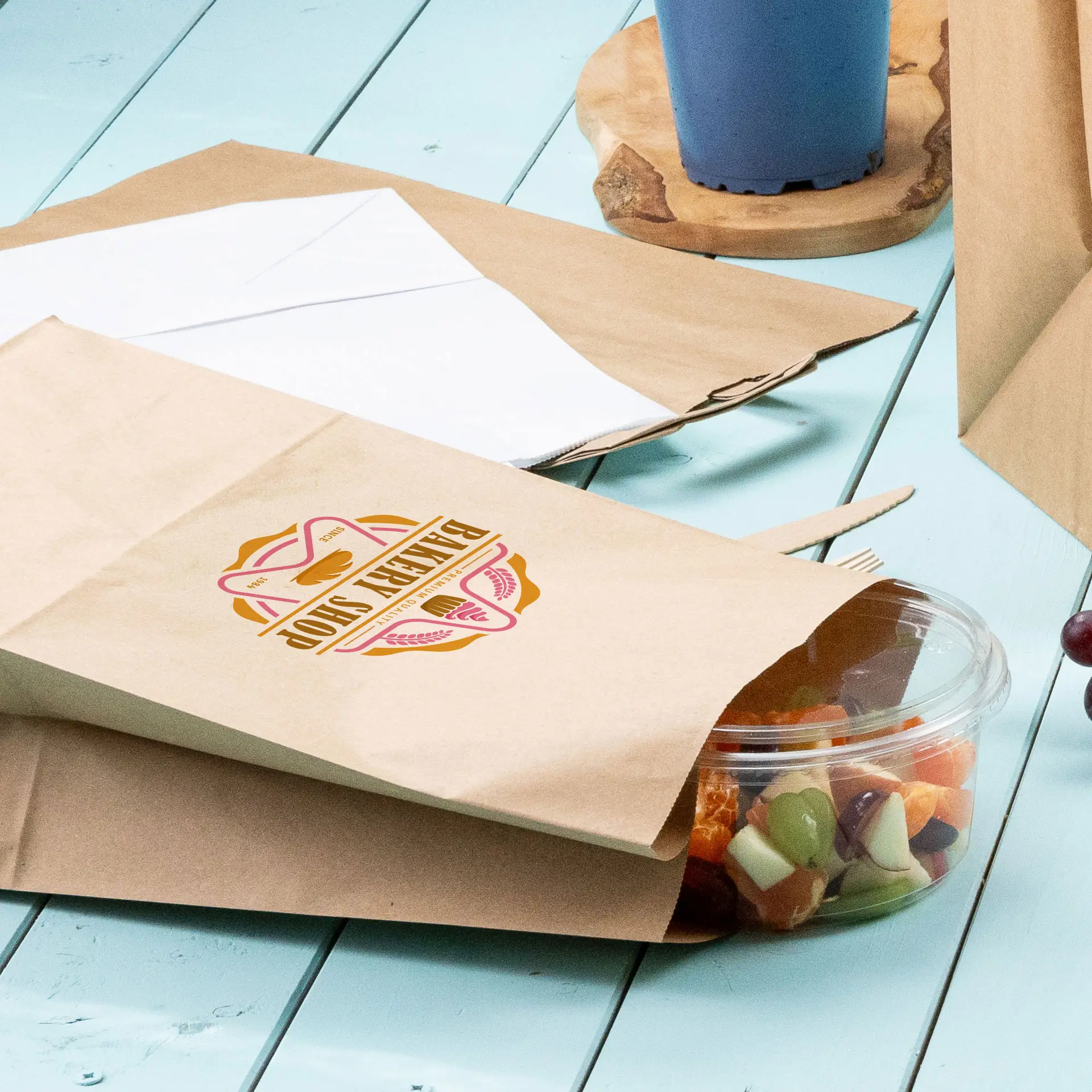 Busta di carta marrone stampata con un design circolare verde, parzialmente aperta con un contenitore trasparente di frutta mista accanto.