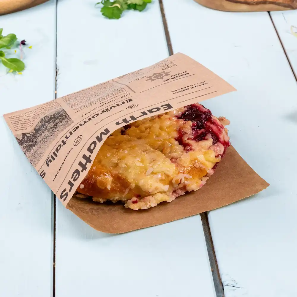Un prodotto da forno con ripieno di frutta, parzialmente avvolto in una borsa di carta marrone con un'etichetta stampata.