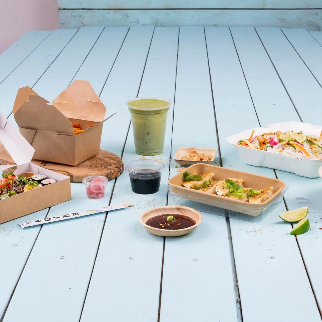 Varietà di cibi asiatici su un tavolo di legno blu, tra cui sushi, ravioli, insalata e una bevanda verde.