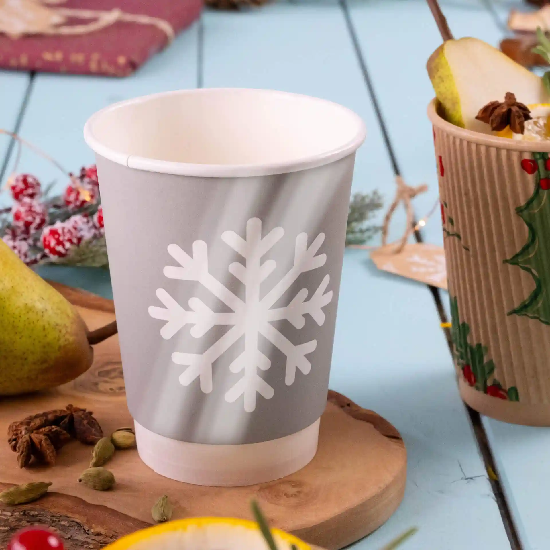 Bicchiere di carta grigio con design di fiocco di neve bianco, a doppia parete, su una superficie di legno con una pera e spezie vicine.