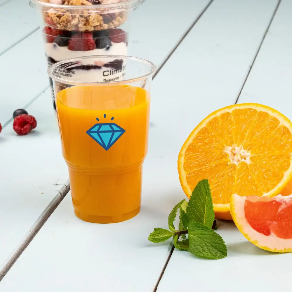Bicchiere di plastica trasparente con succo d'arancia e un motivo a diamante blu, accompagnato da un'arancia affettata e foglie di menta.