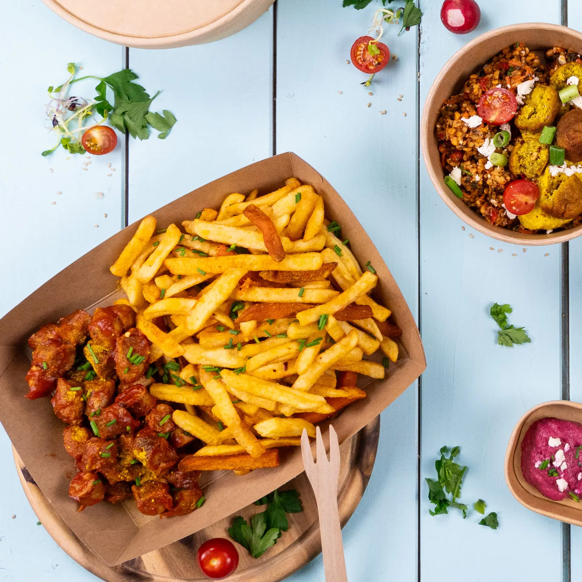 Una porzione di patatine e piatto di carne in un resistente vassoio di cartone marrone; una ciotola di insalata e pomodorini sono nei dintorni.