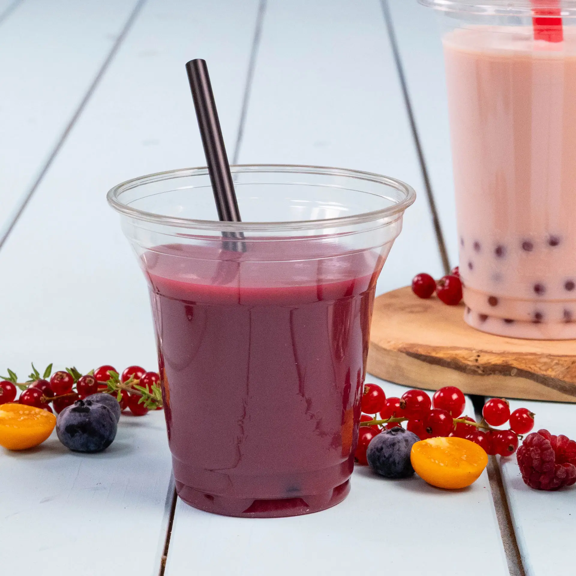 Un bicchiere trasparente riempito di succo rosso scuro e una cannuccia nera; guarnito con frutti di bosco e metà di un frutto giallo.