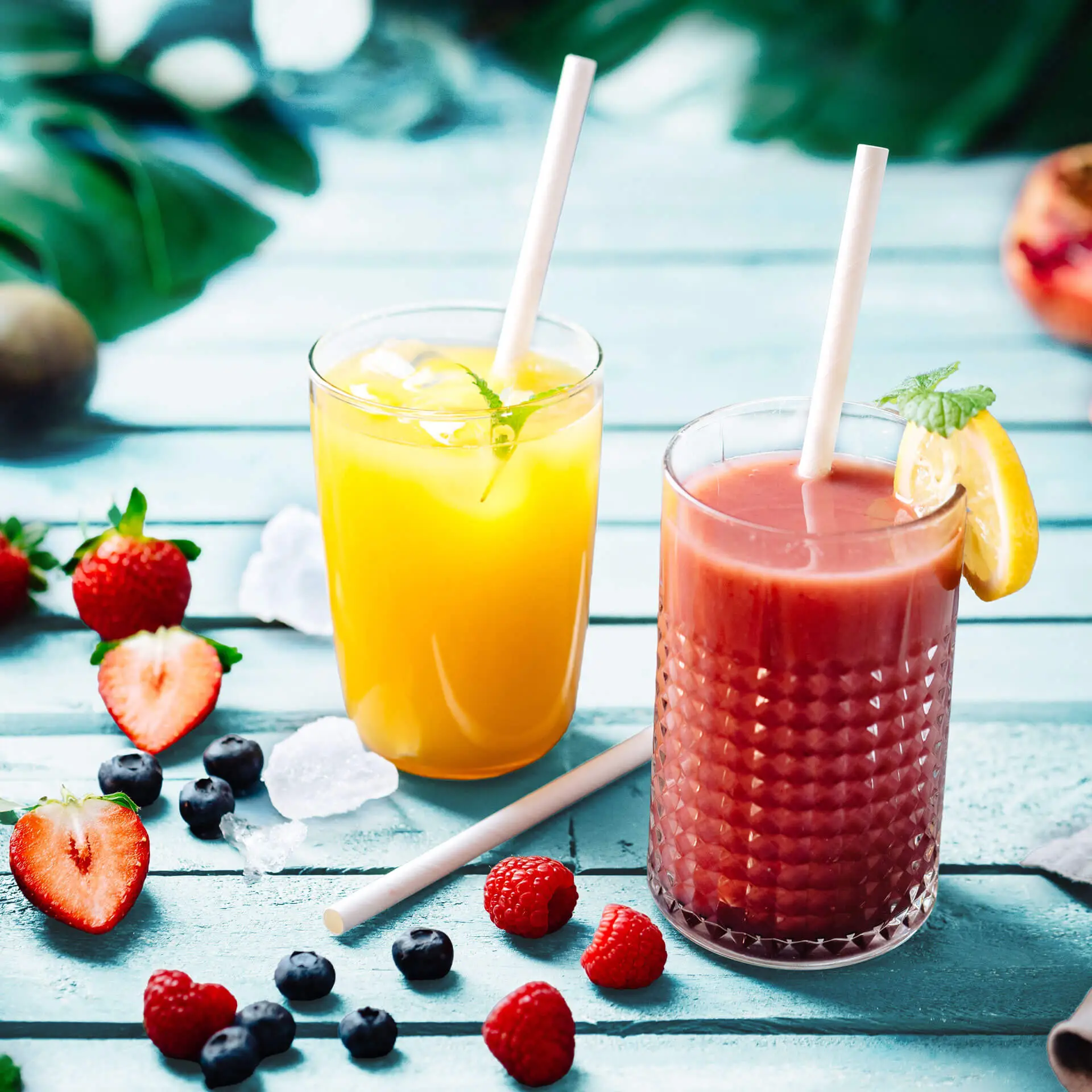 Due bevande in bicchieri trasparenti con cannuccia jumbo bianca; una bevanda gialla con menta e ghiaccio, una bevanda rossastra con una fetta di limone.