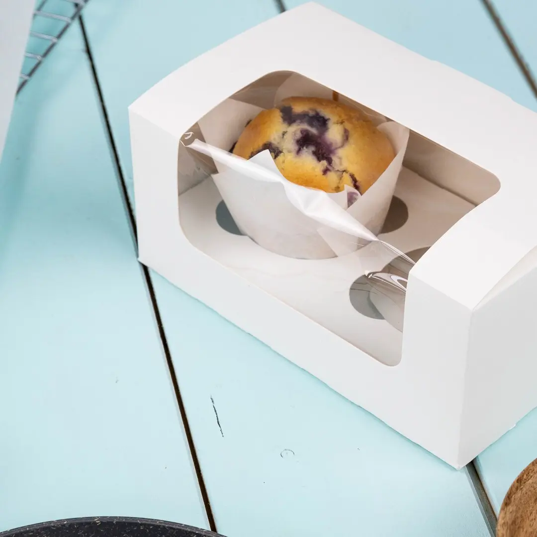 Scatola bianca per cupcake con una finestra trasparente che mostra un muffin ai mirtilli all'interno.