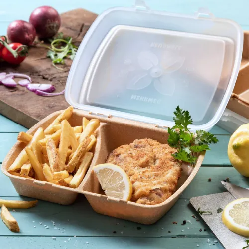 Contenitore con pollo fritto, fettina di limone e patatine, circondato da alimenti e un tagliere.