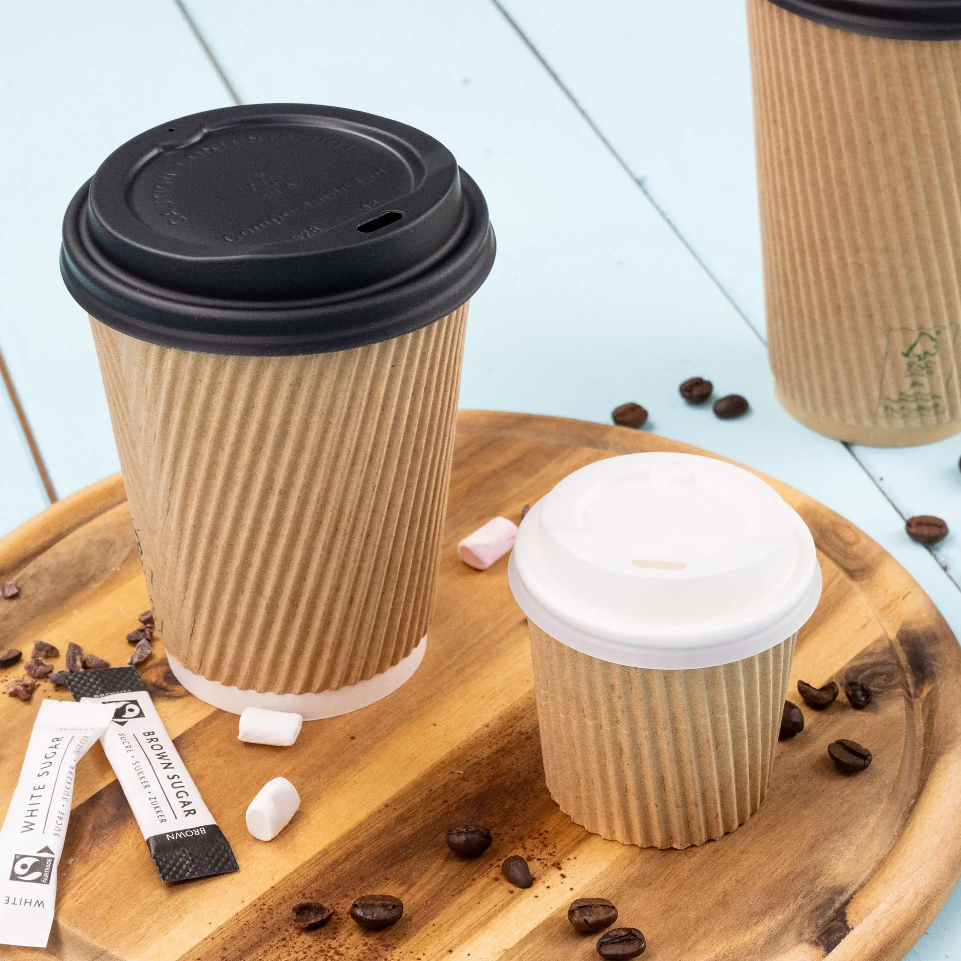 Immagine di due tazze di caffè rigate su una superficie di legno, una marrone con un coperchio nero e una piccola marrone con un coperchio bianco, circondate da chicchi di caffè e bustine di zucchero.