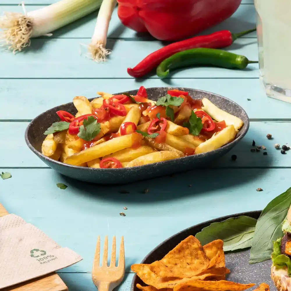 Ciotola di patatine fritte con peperoncini a fette e coriandolo su un tavolo di legno blu.