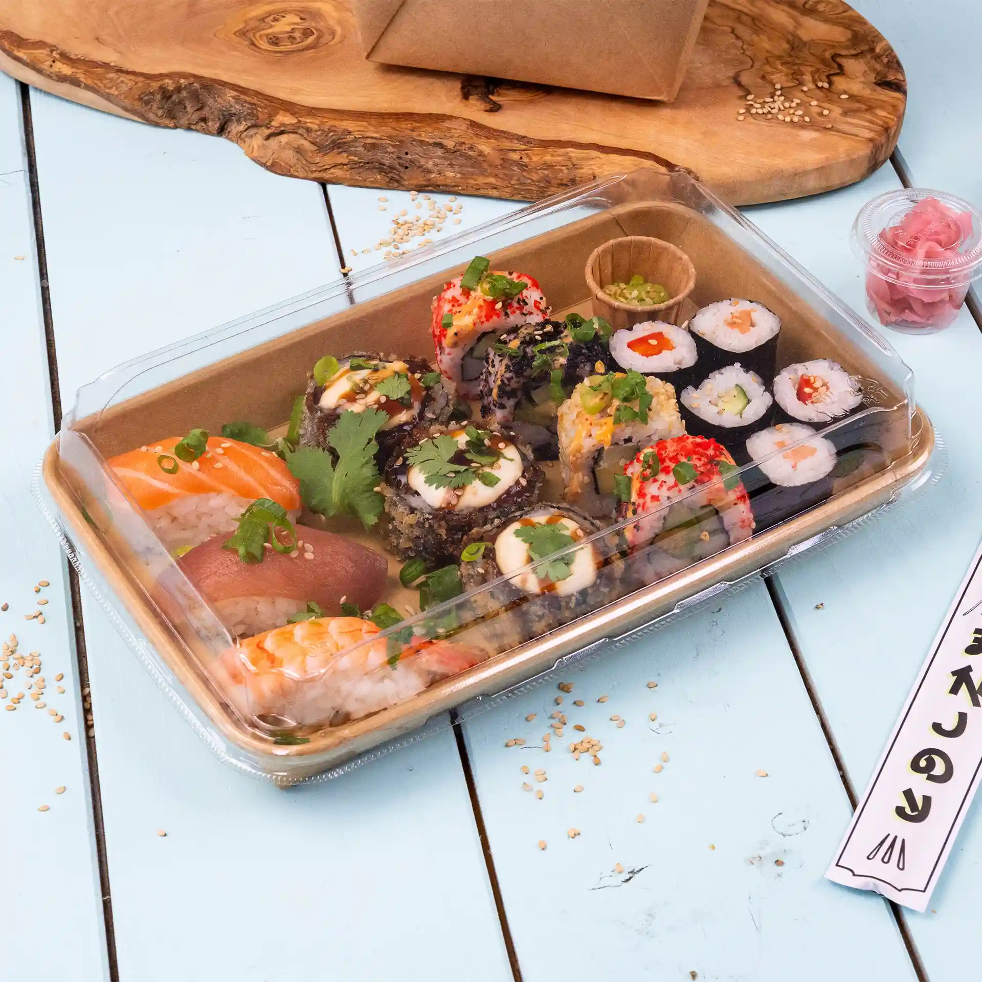 Coperchio trasparente per scatola di sushi con rotoli di sushi assortiti, tra cui salmone e tonno, guarniti con erbe e serviti con zenzero marinato.