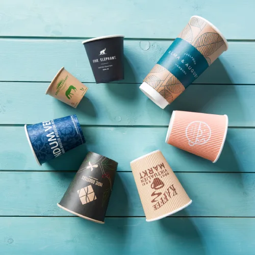 Vari cup in plastica usa e getta con design unici sparsi su una superficie in legno turchese.