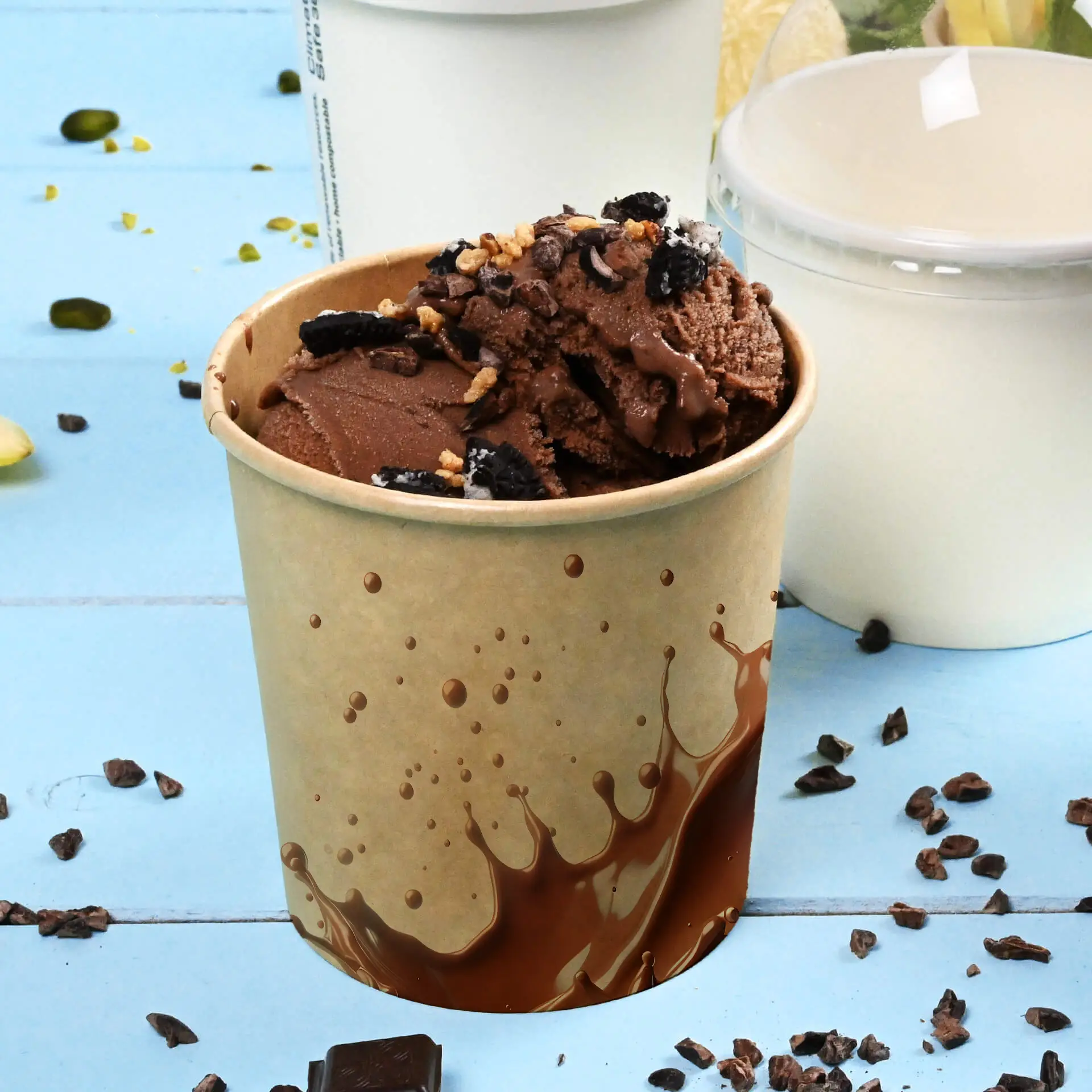 Becher riempito di gelato al cioccolato guarnito con condimenti, posato su una superficie blu con pezzi di cioccolato sparsi.