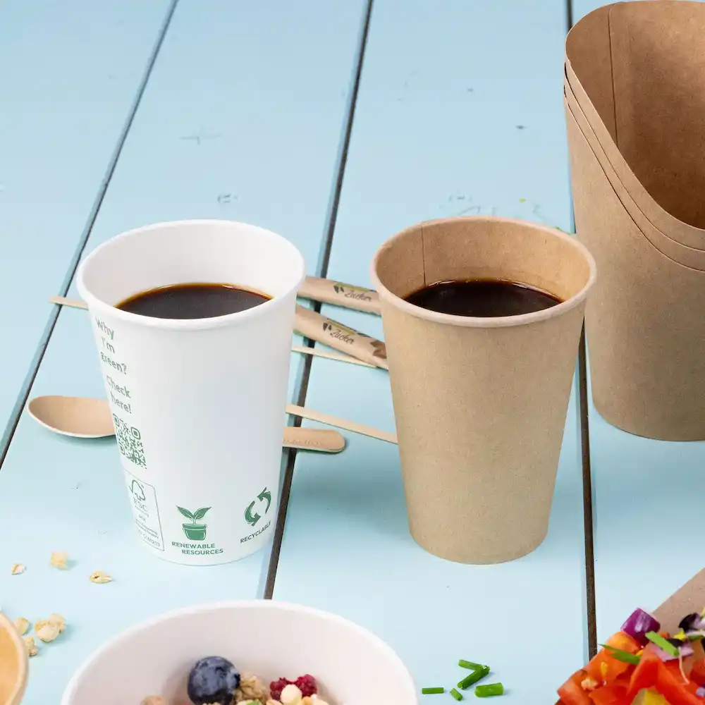 Due tazze con caffè, una bianca e una marrone, accanto a stecchetti di legno su una superficie blu.